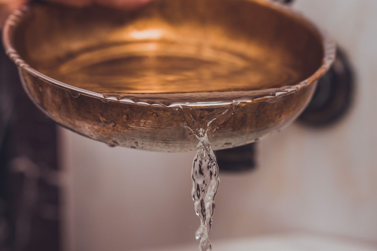 A steady stream of liquid pouring from a traditional bowl, the principle behind Shirodhara