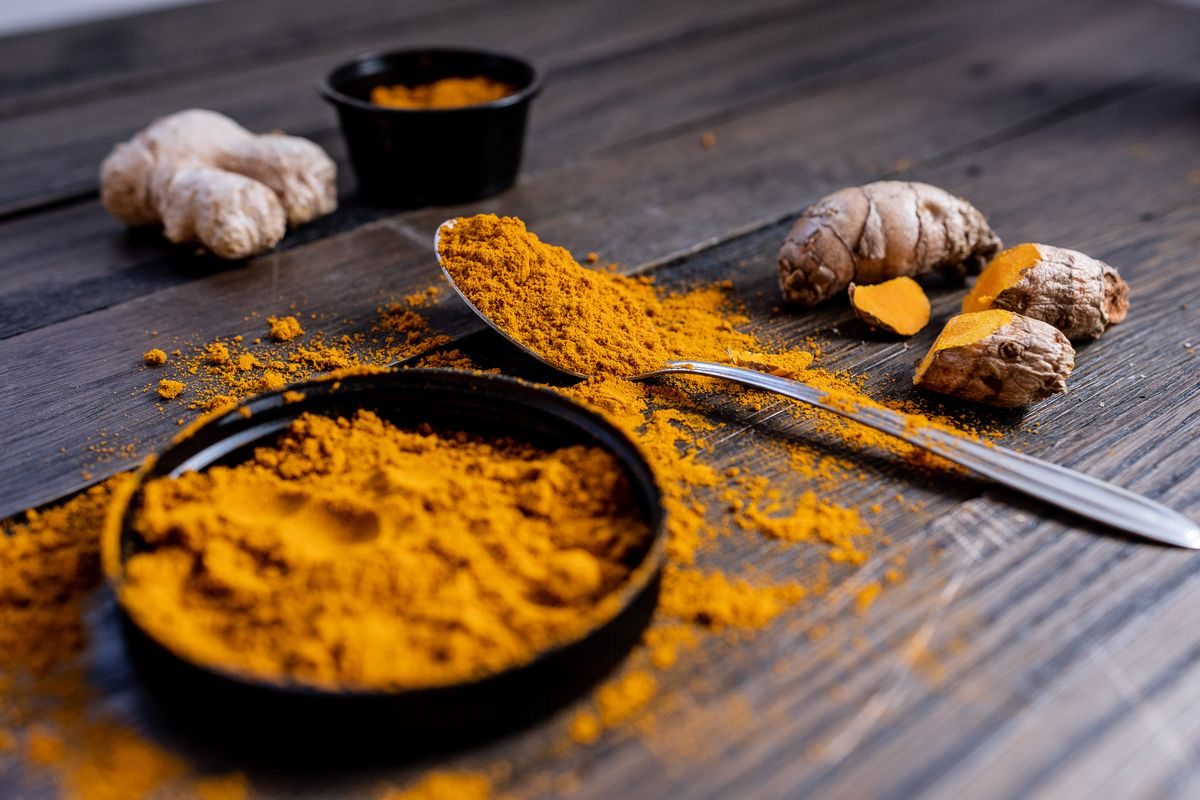 Turmeric powder, fresh turmeric root and ginger on a wooden table
