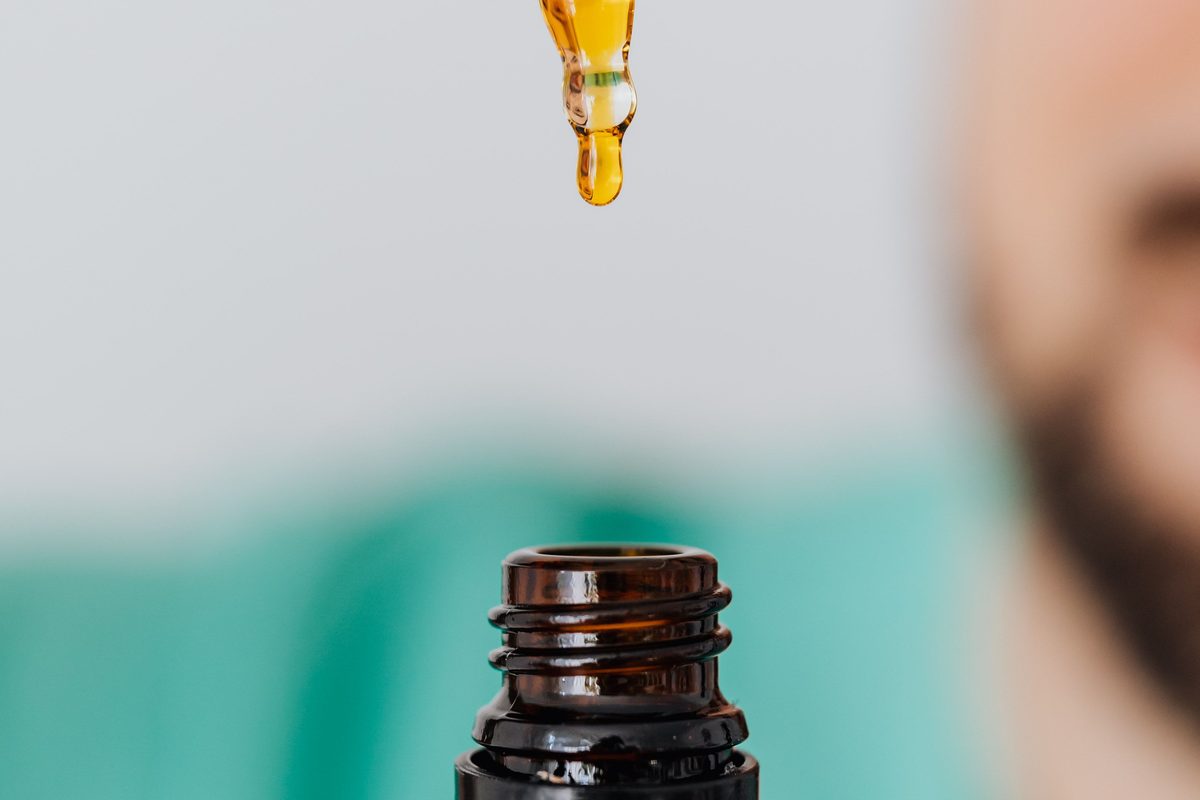 Glass dropper holding golden medicated oil above an open amber bottle