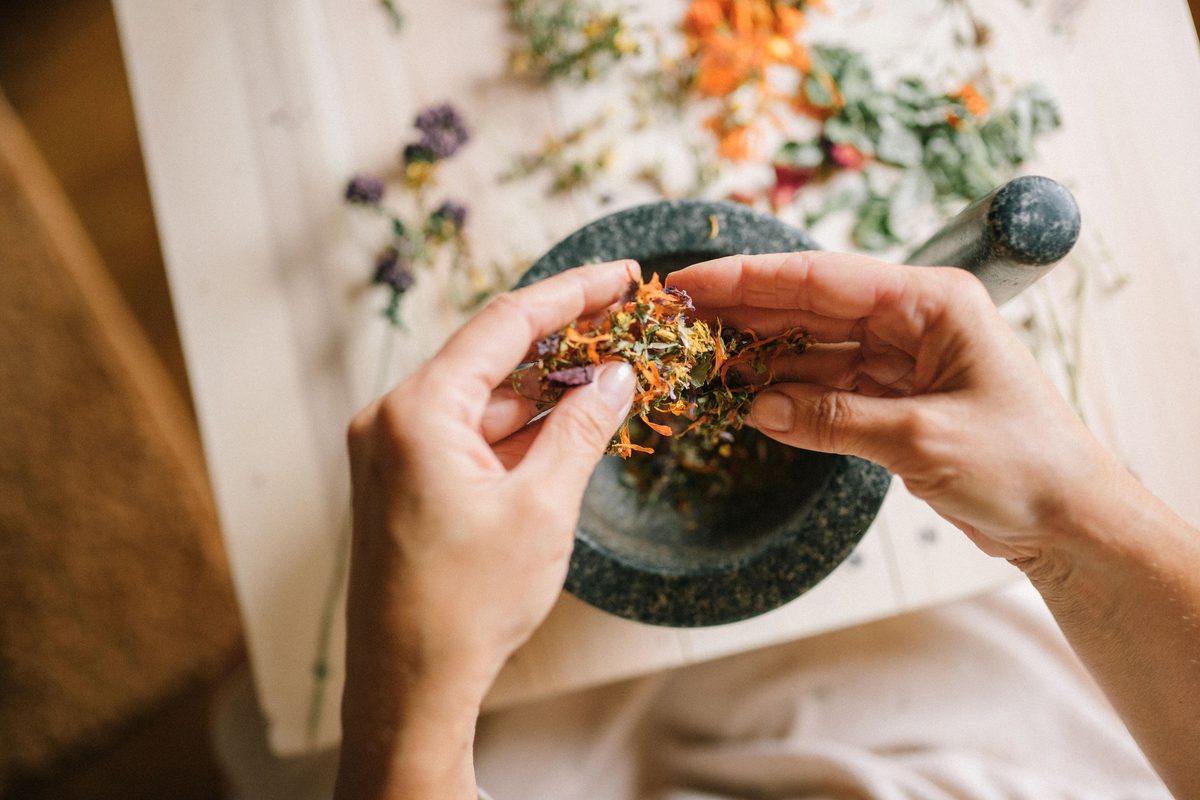 Hands crushing dried herbs and flowers in a stone mortar on a wooden table