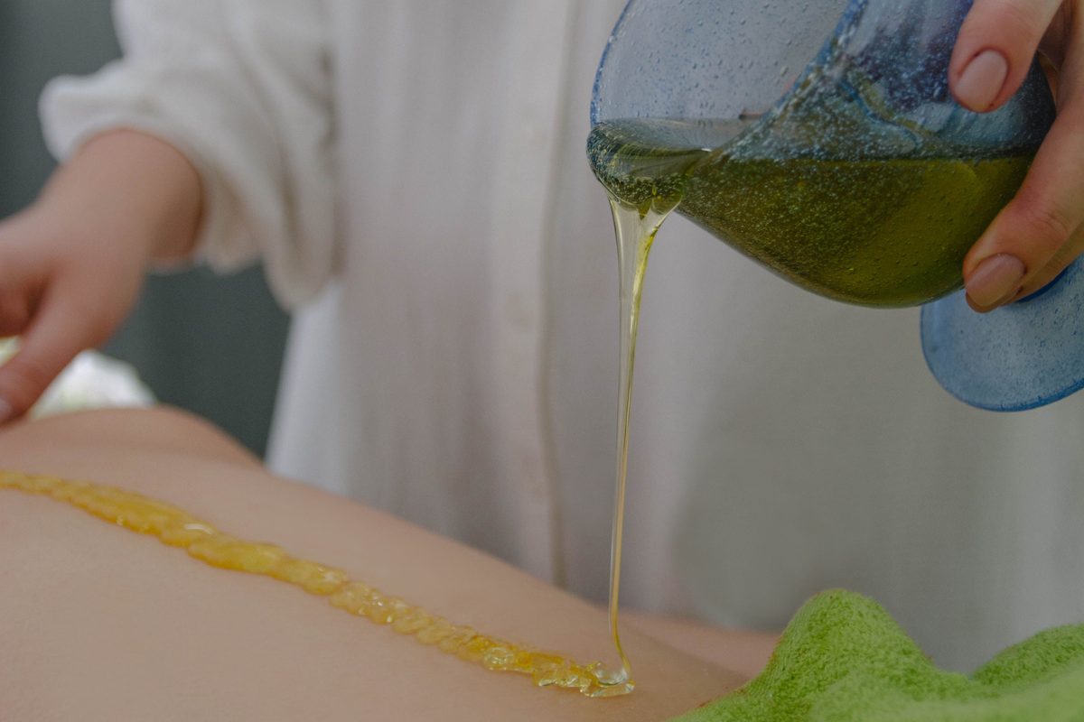Therapist pouring warm green medicated oil onto a patient's back during Panchakarma preparation